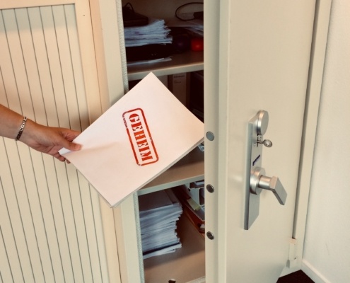 Een persoon legt een document waar 'geheim' op staat in een kluis.