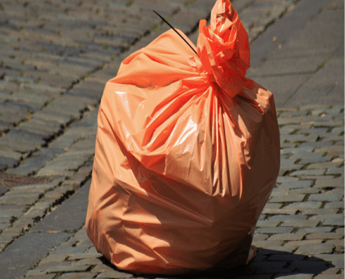 Foto van een oranje vuilniszak op straat.
