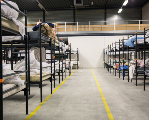 Foto van maatschappelijke opvang locatie Zilverstraat. In een loods staan links en rechts rijen met stapelbedden.