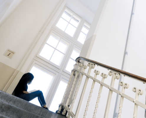 Jongere zit op de grond een boek te lezen in een trappenhuis