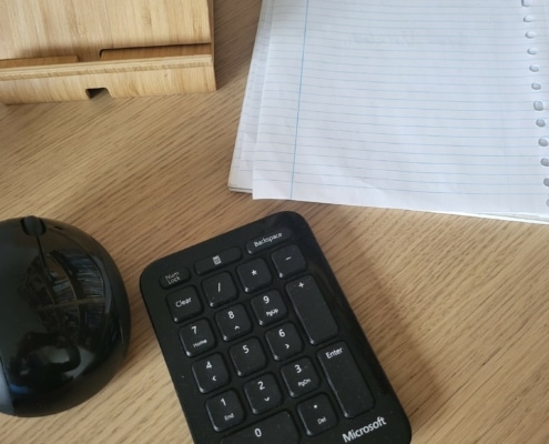 Op een bureau liggen een tabletstandaard, schrijfblok, muis en toetsenbord.