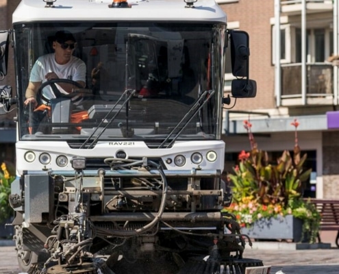 Een medewerker van de gemeente ruimt met een schoonmaakwagen straatafval op.