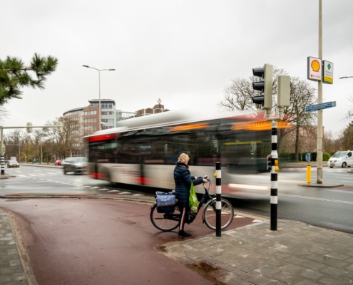 Foto van kruispunt van Alkemadelaan / Wassenaarseweg na de wegwerkzaamheden. Een fietser wacht bij een stoplicht terwijl er een bus langsrijdt.